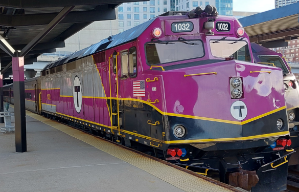A purple MBTA train number 1032. Has Black, gold and grey accents, the MBTA logo on the side and front, and an American flag under the engineer's side window.